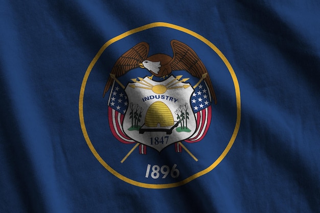 Utah US-Staatsflagge mit großen Falten, die in der Nähe unter dem Studiolicht im Innenbereich winken Die offiziellen Symbole und Farben im Banner