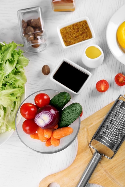 Utensilios de cocina e ingredientes para ensalada en mesa sobre fondo claro