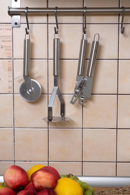 Utensilios de cocina en forma de abrelatas, machacador de papas y cortador de pizza cuelgan de ganchos en la pared de la cocina