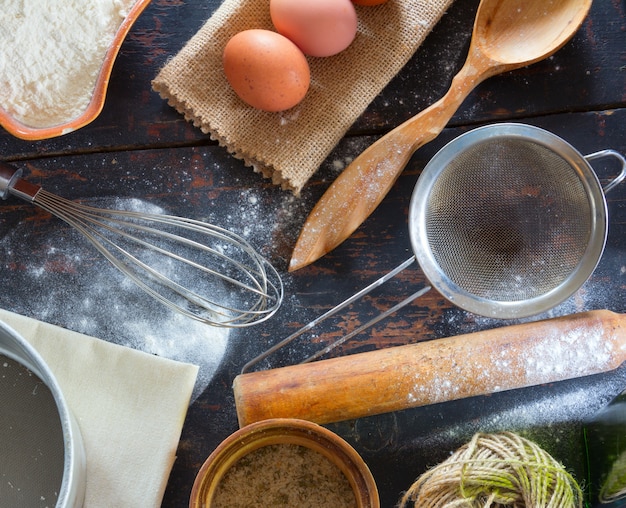 Utensilios de cocina, harina y huevos en la vieja mesa de la cocina, primer plano de la vista superior.