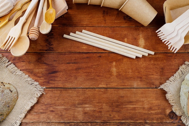 Utensilios de cocina de madera diferentes en la mesa de madera. Cubiertos de madera sobre tablones viejos. Pajitas de bambú y vasos de papel desechables. Vajilla ecológica. Concepto de desperdicio cero. Vista superior