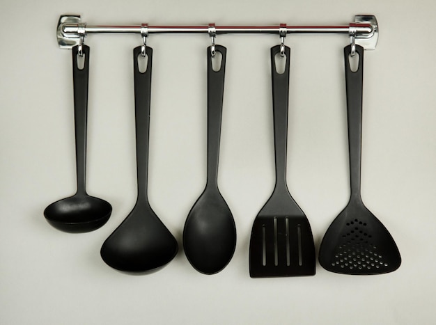 Utensilios de cocina negros en ganchos de plata sobre fondo gris