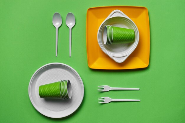 Utensílios de mesa descartáveis de plástico coloridos sobre fundo verde com espaço de cópia o conceito de piquenique uten