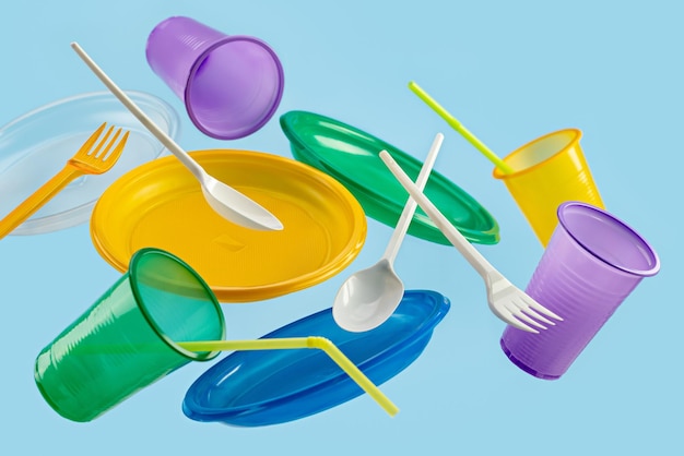 Utensílios de mesa plásticos descartáveis multicoloridos voadores em um fundo azul o conceito de ecologia e r