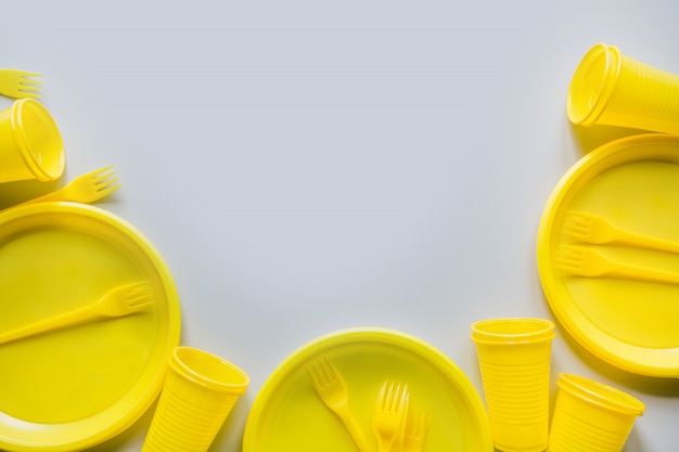 Foto utensilios de picnic de un solo uso amarillos, platos, tazas, tenedores en gris.