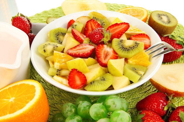 Útil ensalada de frutas de frutas frescas y bayas en un tazón sobre una servilleta aislado en blanco