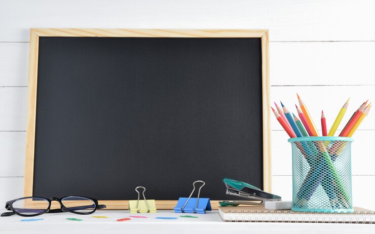 Útiles escolares sobre tablero negro y madera blanca.