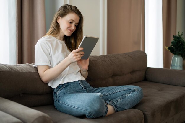 Utiliza una aplicación de tableta y un sitio de Internet. Joven mujer independiente que aprende en línea la educación en el hogar.