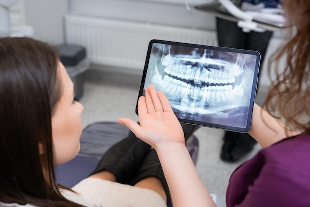 Foto utilizando una tableta para mostrar la imagen de rayos x, la dentista discute las estrategias de tratamiento