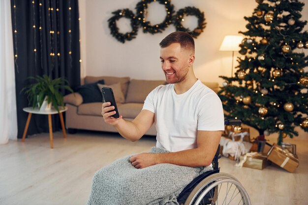 Utilizando el teléfono inteligente para comunicarse con la gente El nuevo año se acerca El hombre discapacitado en silla de ruedas está en casa