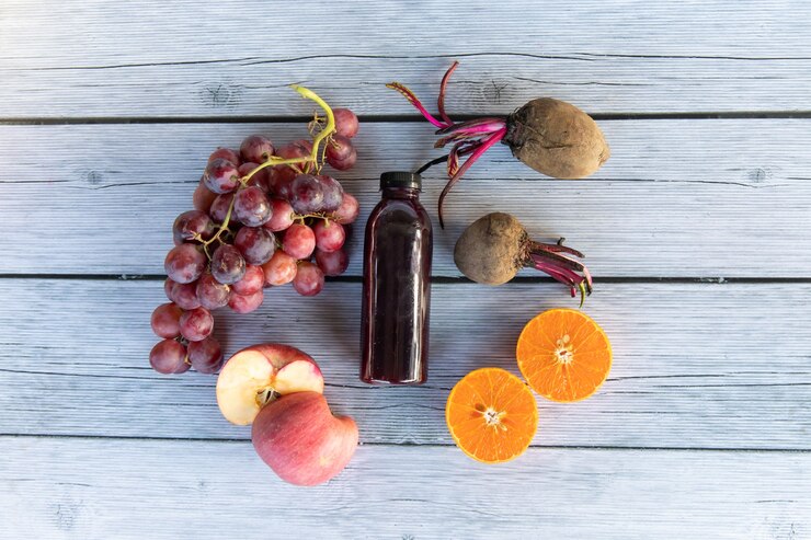 Foto uva o uva de vino con manzana naranja y remolacha coldpressed en jugo de uva saludable en una botella sobre placa de madera