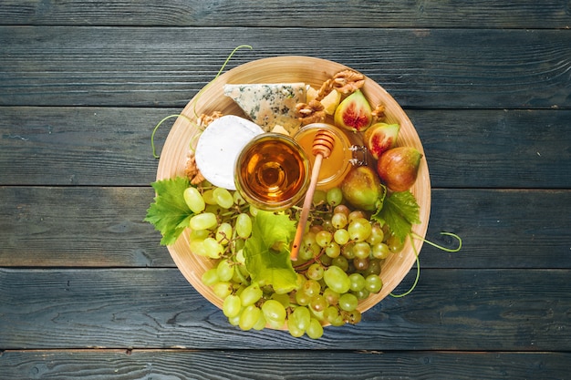 Uva, queso, higos y miel con vino en mesa de madera