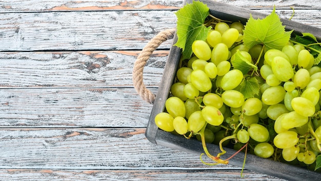 Uvas blancas en una caja de madera sobre una mesa de madera blanca Hojas de uva Vista superior Espacio libre para texto