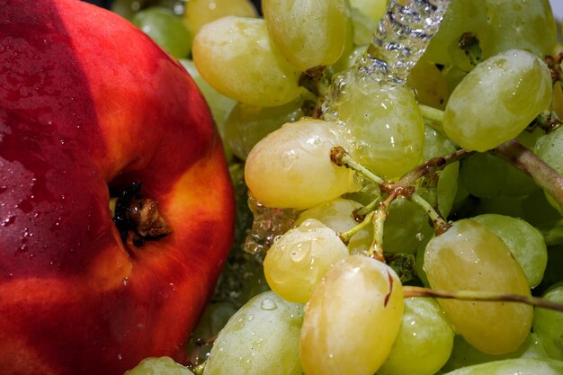 Uvas blancas sin semillas en un racimo y nectarina bajo un chorro de agua limpia fotografía macro de cerca