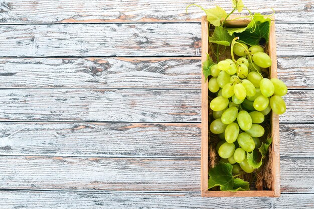 Uvas brancas em uma caixa de madeira em uma mesa de madeira branca Folhas de uvas Vista superior Espaço livre para texto