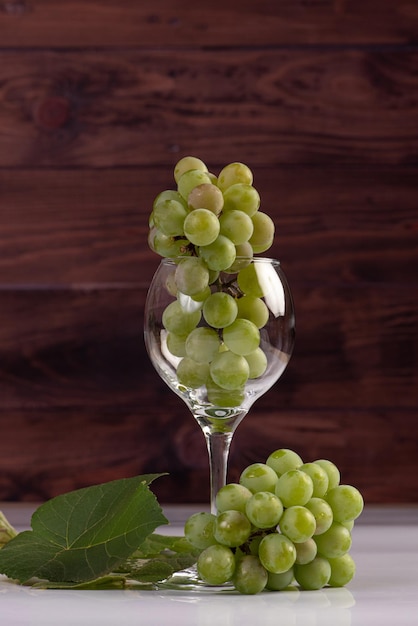 Uvas, cachos de uvas verdes colocados junto com uma cesta de palha e uma tigela na superfície branca, foco seletivo.