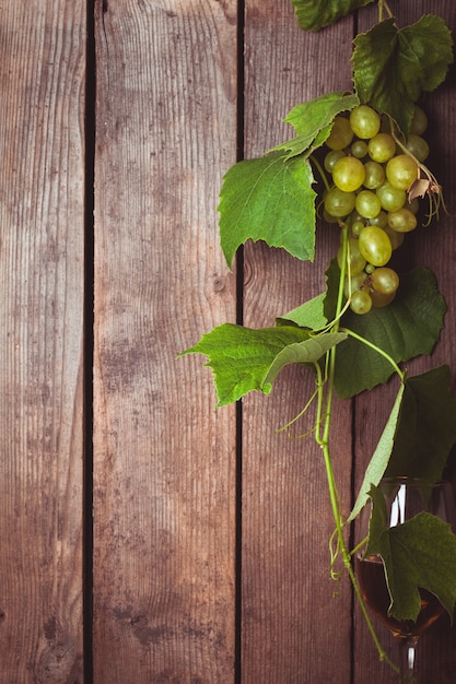 Uvas com folhas e copo de vinho no fundo de madeira