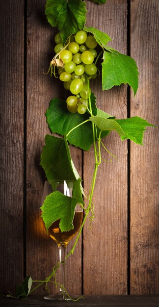 Uvas com folhas e copo de vinho no fundo de madeira