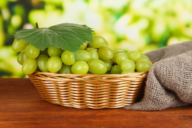 Uvas deliciosas maduras em uma cesta de vime na mesa sobre fundo brilhante