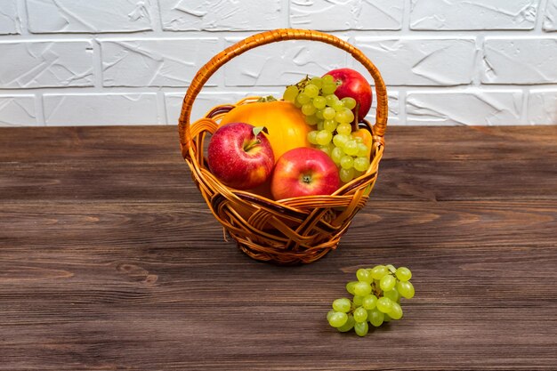 Uvas e maçãs em uma cesta de vime em uma mesa de madeira Conceito de colheita Lugar para uma inscrição