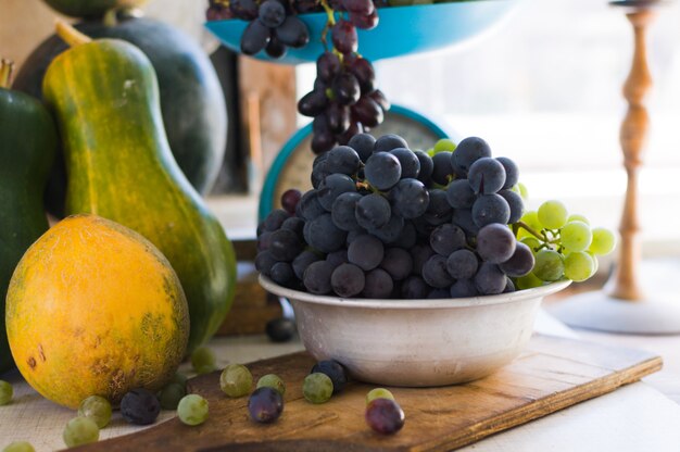 Uvas em uma tigela de metal, uvas são espalhadas sobre uma mesa de madeira branca. conceito de colheita de outono.