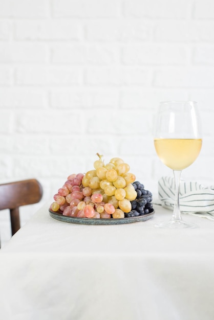 Las uvas frescas están sobre la mesa con una copa de vino blanco en un fondo claro