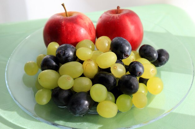 Uvas frescas y manzanas en plato de vidrio