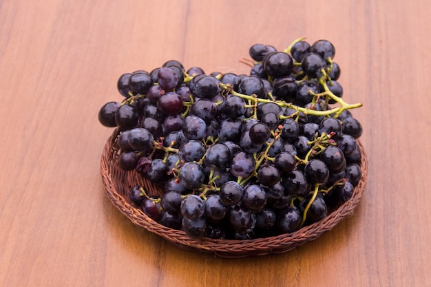 Uvas maduras en canasta de mimbre sobre mesa de madera