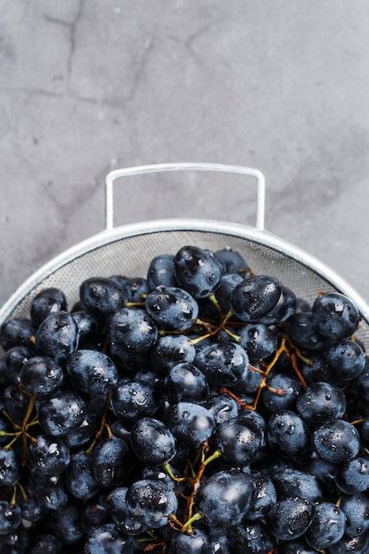 Uvas maduras e pretas em uma tigela de metal em um fundo preto. Vista do topo