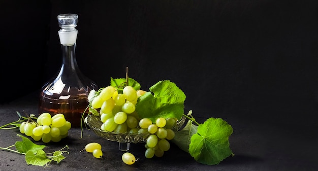 Uvas maduras frescas en un frutero y decantador con jugo de uva sobre fondo negro. Copia espacio