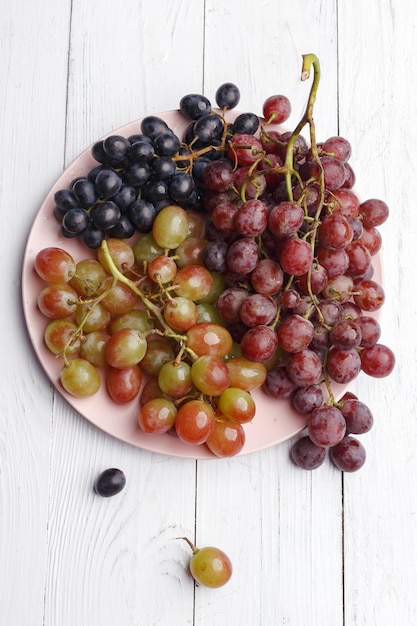 Uvas maduras jugosas en un plato sobre una madera blanca. Vista superior.