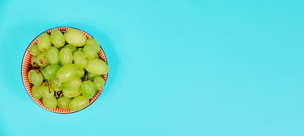 Uvas de mesa verdes en un tazón sobre fondo azul. Dieta saludable