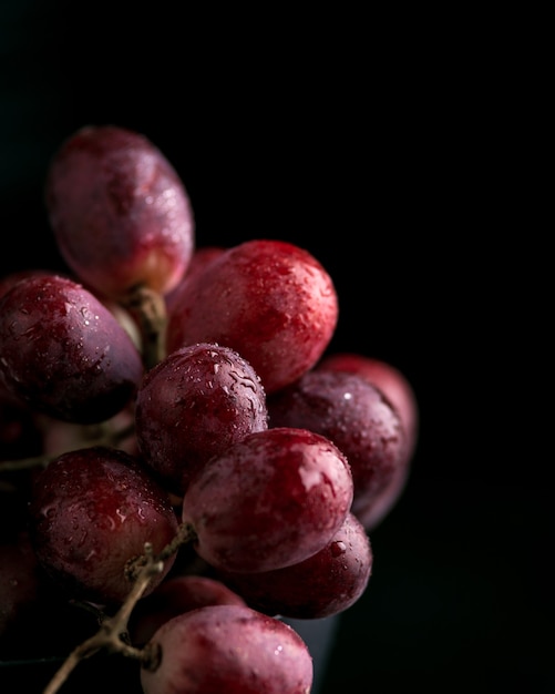 Uvas moradas con gotas de agua, jugo de uva en un frasco de vidrio, imagen oscura. Enfoque seleccionado, macro.