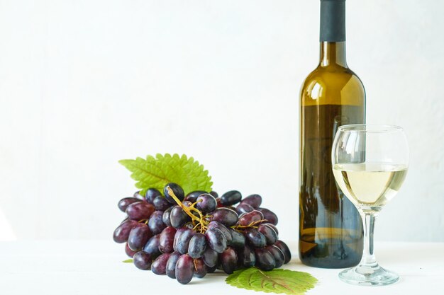 Uvas negras con una copa de vino blanco y una botella de vino en una mesa de luz