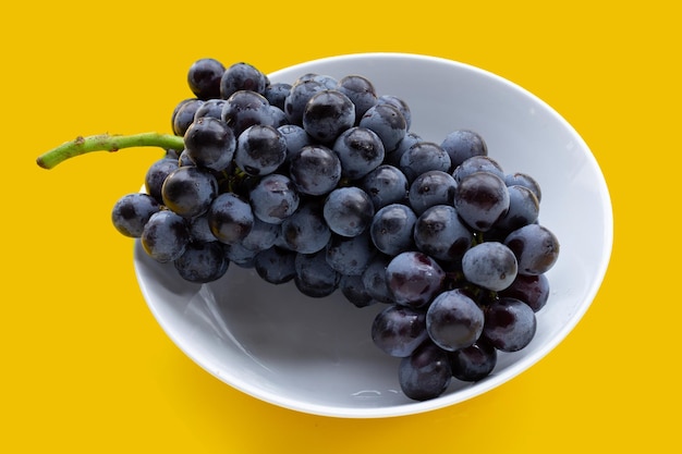 Uvas negras frescas en un tazón sobre fondo amarillo.