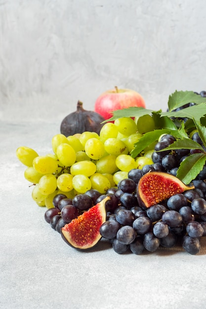 Uvas negras y verdes, higos y hojas sobre una mesa gris.