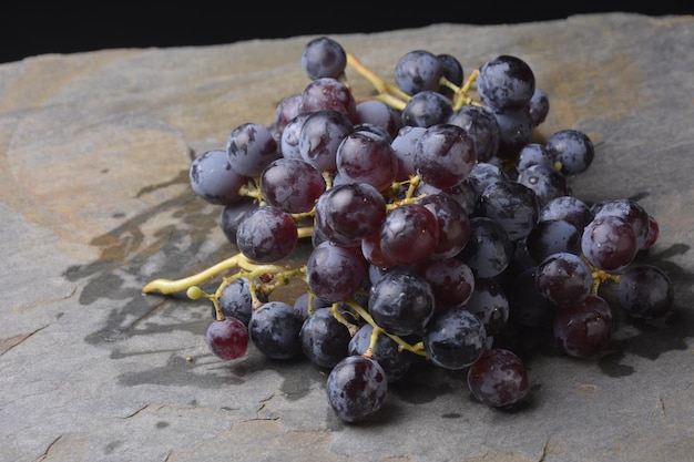 Uvas recién cortadas sobre losa de piedra pizarra y fondo negro.