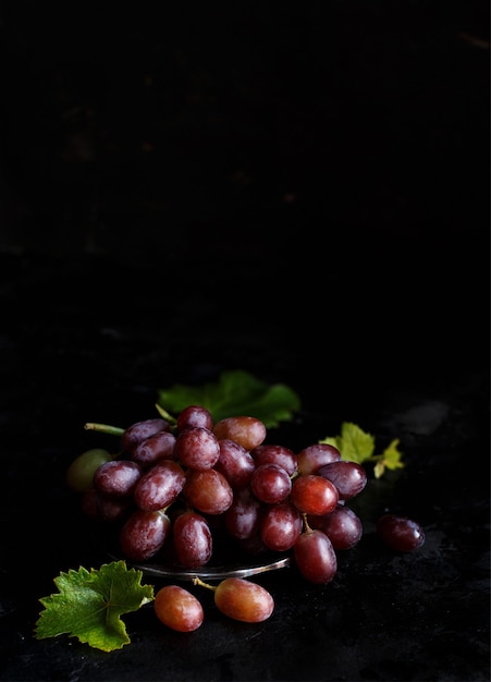 Uvas rojas en un recipiente de plata sobre un fondo oscuro