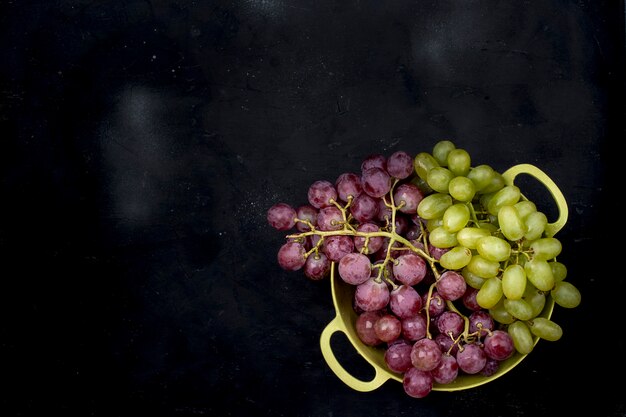 uvas rosadas y verdes en un recipiente sobre un fondo negro