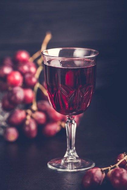 Uvas roxas com suco de uva em uma jarra de vidro, imagem escura.