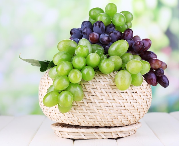 Uvas verdes e roxas maduras na cesta na mesa de madeira no fundo natural