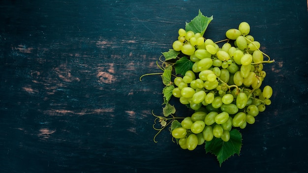 Uvas verdes frescas com folhas de uvas Vista superior em um fundo preto de madeira Espaço livre para texto