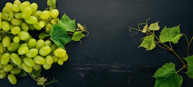 Uvas verdes frescas com folhas de uvas Vista superior em um fundo preto de madeira Espaço livre para texto