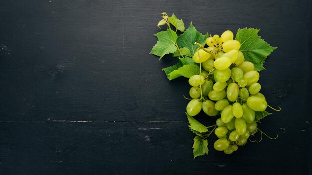 Uvas verdes frescas con hojas de uva Vista superior Sobre un fondo de madera negra Espacio libre para texto