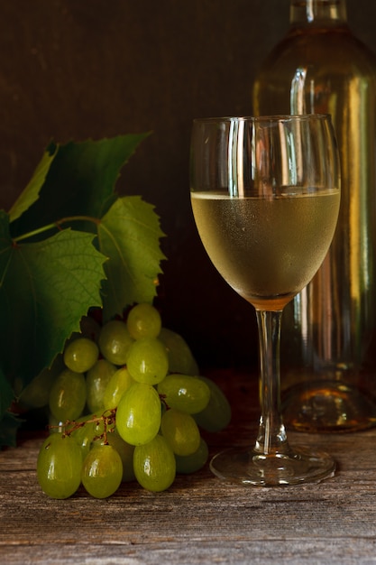 Uvas verdes con hojas, copa, botella de vino blanco.