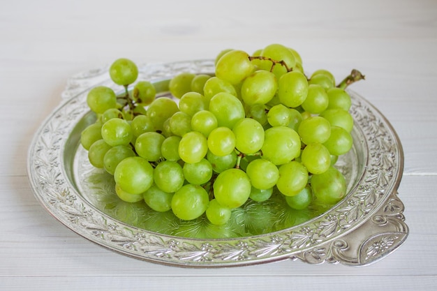Uvas verdes en un plato sobre un fondo blanco de madera