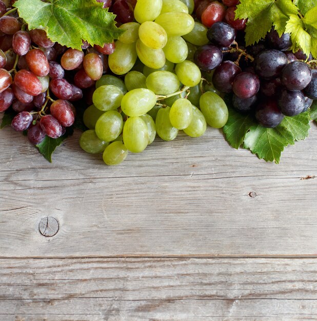 Uvas vermelhas, brancas e azuis com folhas em uma velha mesa de madeira