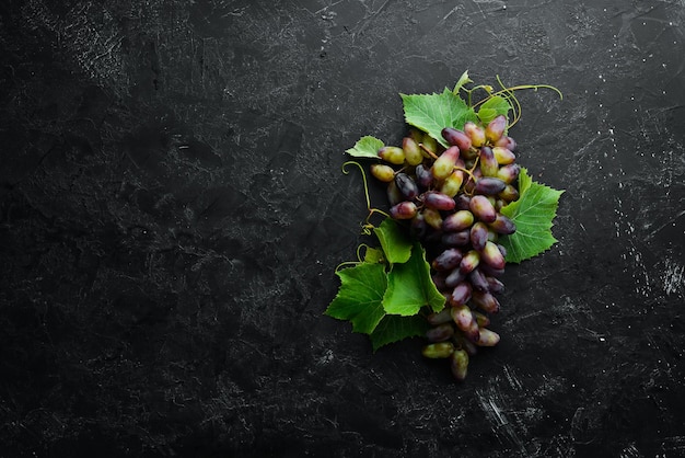 Uvas vermelhas frescas com folhas em uma mesa de pedra preta vista superior espaço livre para o seu texto