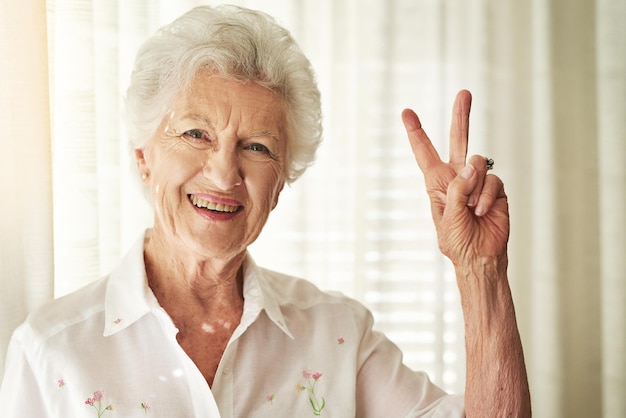 V de vitalidad Retrato de una anciana feliz mostrando un gesto de paz en casa