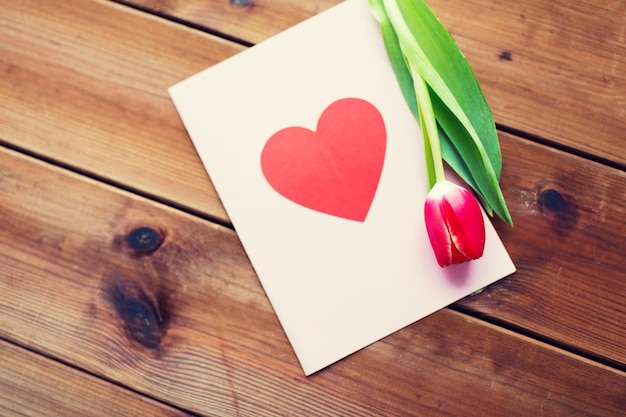 vacaciones, amor y concepto de día de San Valentín - primer plano de flores de tulipán y tarjeta de felicitación con corazón en mesa de madera